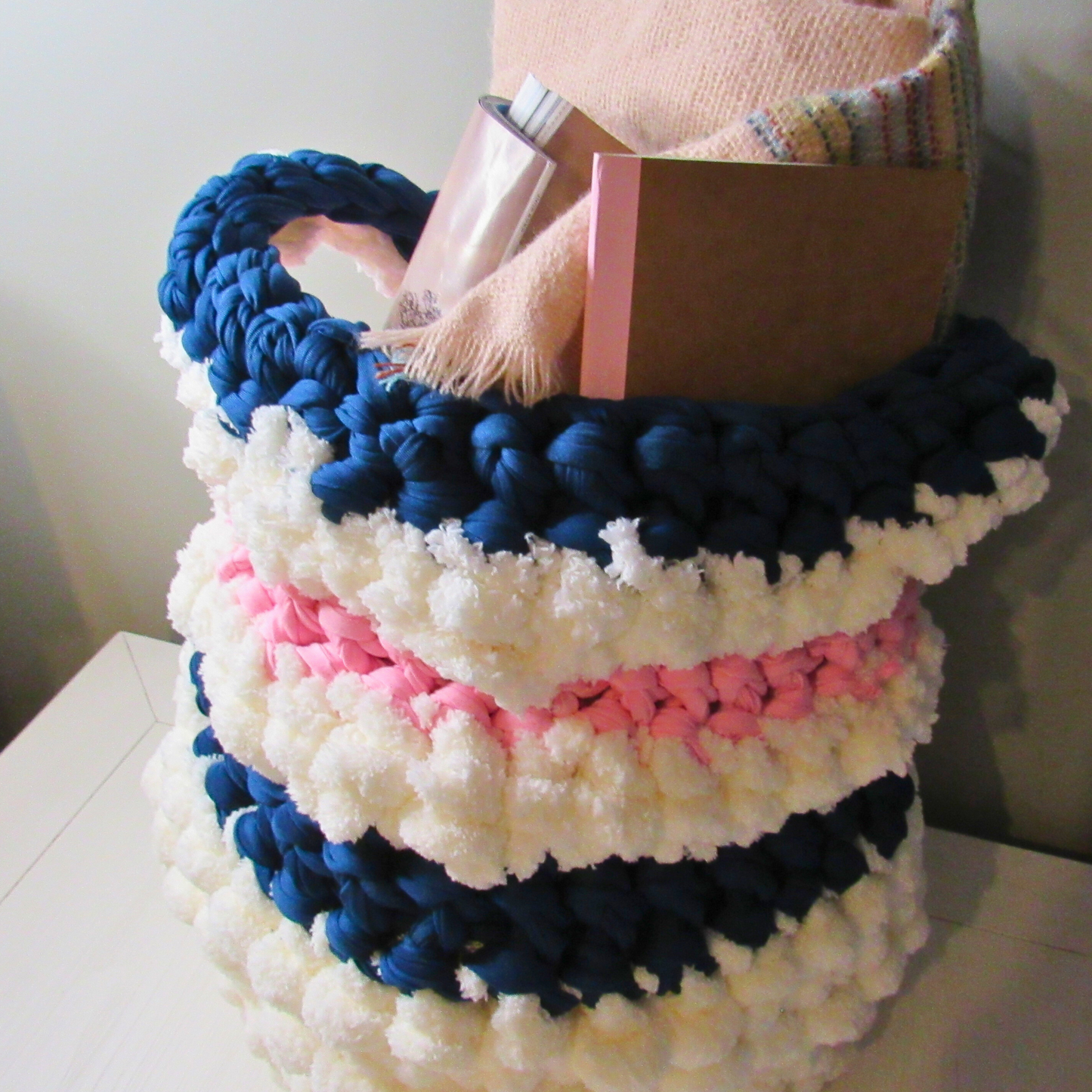 white crocheted storage basket storing a blanket, magazine and a small notebook